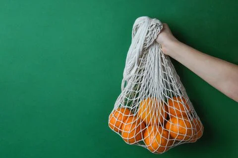 Apples in a string bag in hands on a green background. Stock Photos