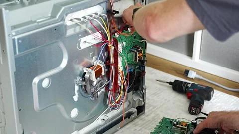 Appliance technician replacing faulty electronic control board inside electric Stock Footage 345658853