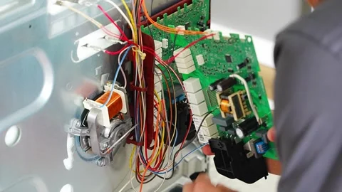 Appliance technician replacing faulty electronic control board inside electric Stock Footage 345659318