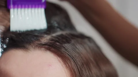 Application of lightening paste closely around hairline, salon technician Stock Footage 330602882