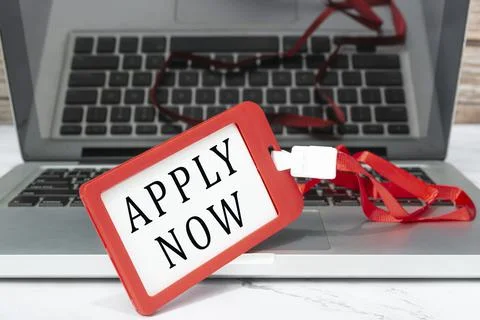 Apply now text written on red name tag placed on a laptop. Foto stock