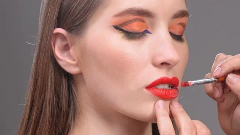 Apply red lipstick with brush in hand of make-up artist. Red lips concept. Young Stock Footage 148270903