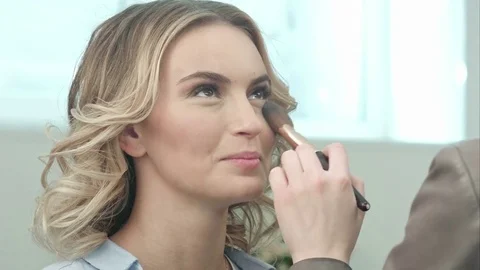 Applying blush makeup with brush to cheekbones of smiling young woman Stock Footage 74660996