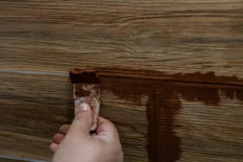 Applying brown grout manually with a small trowel to the joints of wood-look Stock Photos