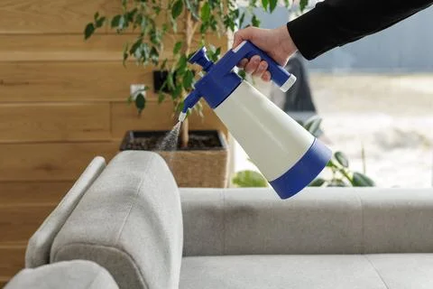 Applying cleaning solution on sofa upholstery with hand pressure sprayer Stock Photos