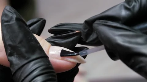 Applying a clear liquid to the nail plate of a finger with a black brush from a Stock Footage 298038992