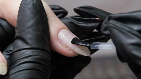 Applying a clear liquid to the nail plate of a finger with a black brush from a 库存影片 333137724