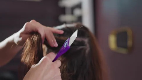 Applying color beneath studio lighting, touching up roots with precise brush Stock Footage 321651636