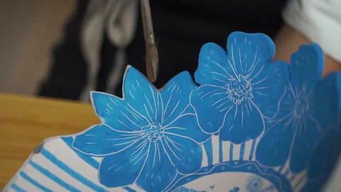 Applying glaze with a brush to the edges of ceramic blue plate. Pottery at home 库存影片 256324319