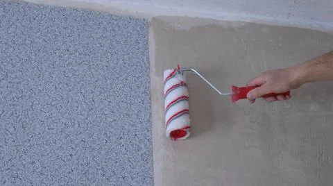 Applying glue with a roller on the wall under the ceiling Stock Photos