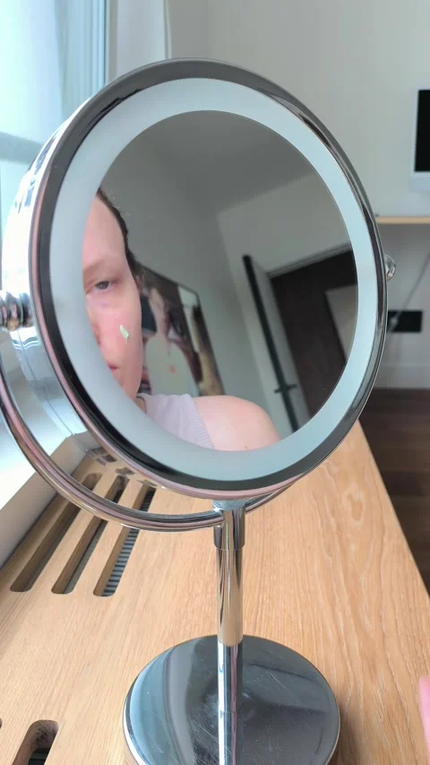 Applying green concealer base on face skin looking into a makeup mirror. Yo.. Stock Footage 345552993