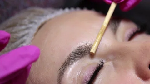 Applying liquid wax to the model's eyebrows with a brush in a beauty salon Stock Footage 156237054