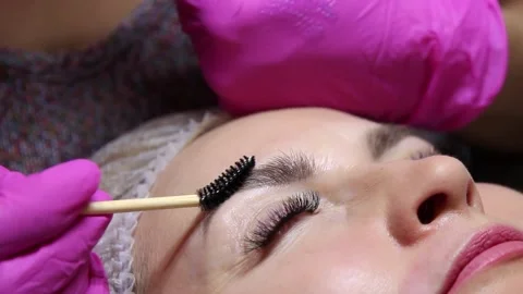 Applying liquid wax to the model's eyebrows with a brush in a beauty salon Stock Footage 156237056