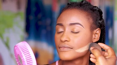Applying makeup powder on face of an african woman Stock Footage 229377167