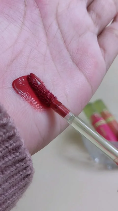 Applying maroon red lip tint on palm using brush applicator. Stockbeeldmateriaal 338401860