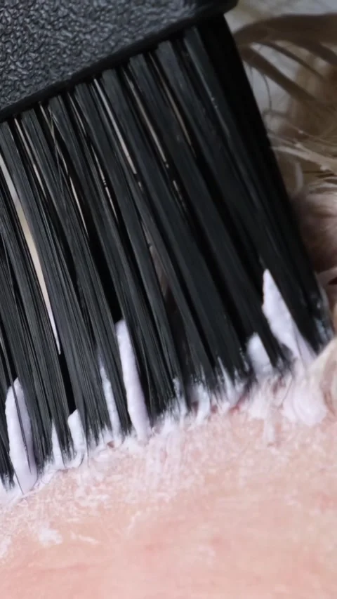 Applying paint to lighten or bleach with a brush on the regrown roots of blond Stock Footage 311511618