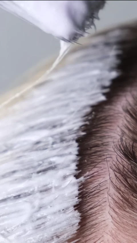 Applying paint to lighten or bleach with a brush on the regrown roots of blond Stock Footage 311511634