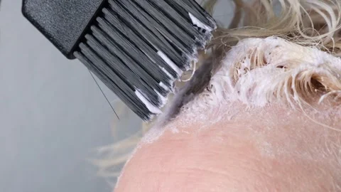 Applying paint to lighten or bleach with a brush on the regrown roots of blond Stock Footage 311512717