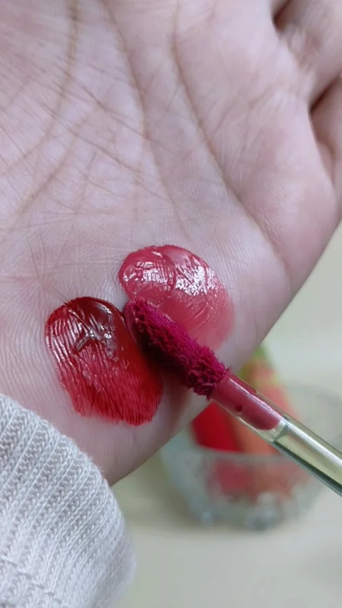 Applying pinkish red lip tint to palm skin using makeup brush. Stockbeeldmateriaal 338401821