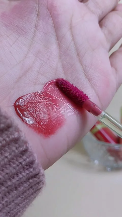 Applying pinkish red lip tint to palm skin using makeup brush applicator. C.. Stock Footage 338984775