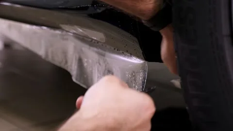 Applying a protective film to the car with tools for work. Car detailing. Stock Footage 312437325