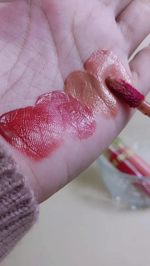 Applying red lip tint on palm using makeup brush applicator. Vertical close up Stockbeeldmateriaal 338401818