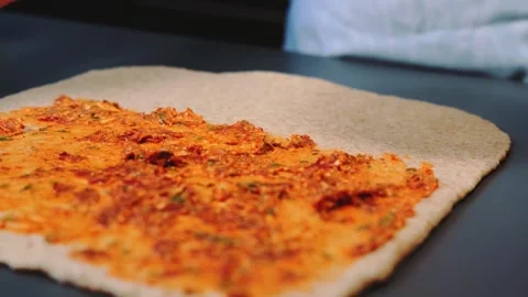 Applying reddish-orange filling on rolled-out dough in kitchen Видео 342869836