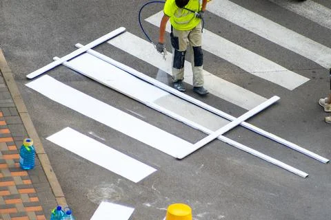 Applying road markings. Paint stray a pedestrian crossing with white paint. Stock Photos