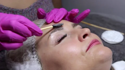 Applying shampoo for eyebrows and eyelashes of the model with a brush in a beaut Stock Footage 156236894