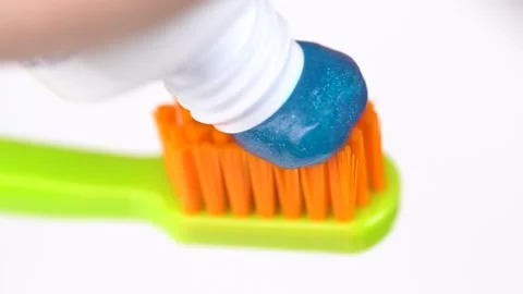 Applying shiny blue toothpaste to a gren and orange toothbrush, macro video.. Stock Footage 278689070