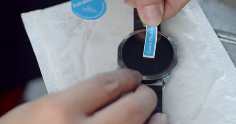 Applying a tempered glass screen protector onto a smartwatch display to prevent  Stock Footage 323344149