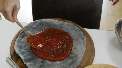 Applying tomato ketchup with metal spoon on pizza base Stock Footage 230119909