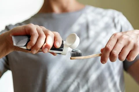 Applying toothpaste on a bamboo tooth brush. Hands squeezing tube with a to.. Stock Photos