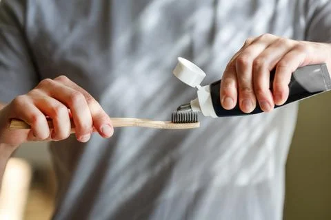 Applying toothpaste on a bamboo tooth brush. Hands squeezing tube with a to.. Stock Photos