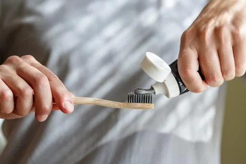Applying toothpaste on a bamboo tooth brush. Hands squeezing tube with a to.. Stock Photos