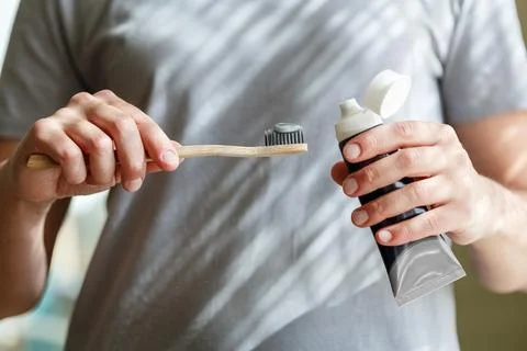 Applying toothpaste on a bamboo tooth brush. Hands squeezing tube with a to.. Stock Photos