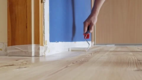 Applying varnish to wooden floor with roller during interior renovation work on Stock Footage 313256520