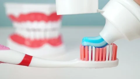 Applying vibrant blue toothpaste on toothbrush with teeth model in background Stock Footage 306297171
