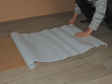 Applying white adhesive paper to a sheet of plywood on a room floor Stock Photos