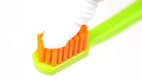 Applying white toothpaste to a gren and orange toothbrush macro video. Dent.. Stock Footage 278689089