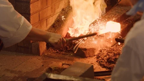 Apprentice black smith adding grass to a glowing hot ingot then back into hot fo Stock-Footage 125429510