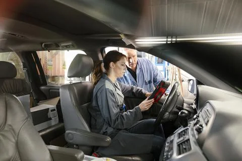 Apprentice car mechanic sitting in driver's seat with computer 스톡 사진