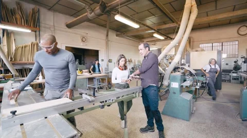 Apprentice carpenter cutting wood with a table saw under supervision Stock Footage 337882299