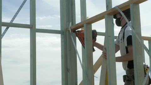 Apprentice Carpenter Uses Nail Gun To Fasten Timber Housing Frame Stock Footage 164623213