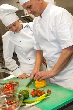 Apprentice learning cutting vegetables from chef Stock Photos