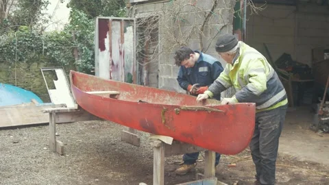An apprentice learns from a carpenter repairing gunwales on a canoe Stock Footage 235890203