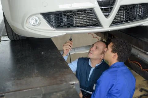 Apprentice mechanic working underneath a car with professor Stock Photos