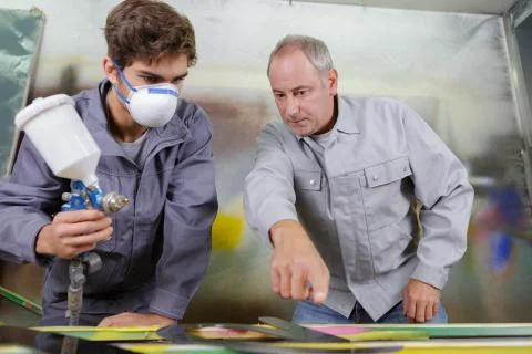 Apprentice painter with airgun spraying paint on a car Stock Photos