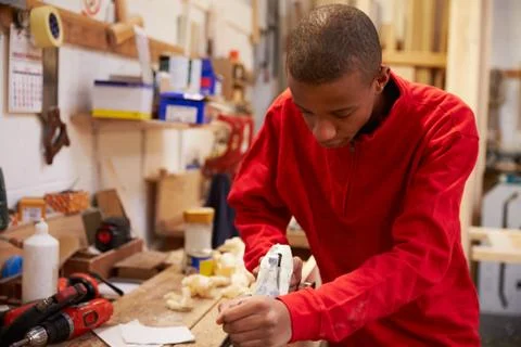 Apprentice Planing Wood In Carpentry Workshop 库存照片