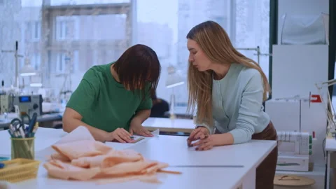 Apprentice Seamstress Measuring and Marking Fabric on a Studio Table with Mentor Video stock 335930743